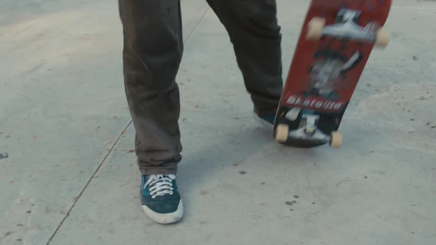 A skateboarder jumps off a short platform in a public park with his skateboard and picks it up to walk away