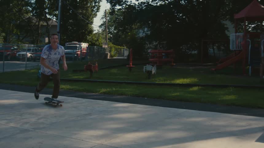 A man rides a skateboard on pavement in an empty playground