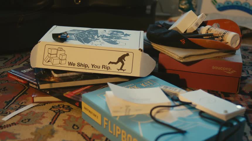 Books shoe boxes and other knick knacks sit in a pile behind a couch in a living room