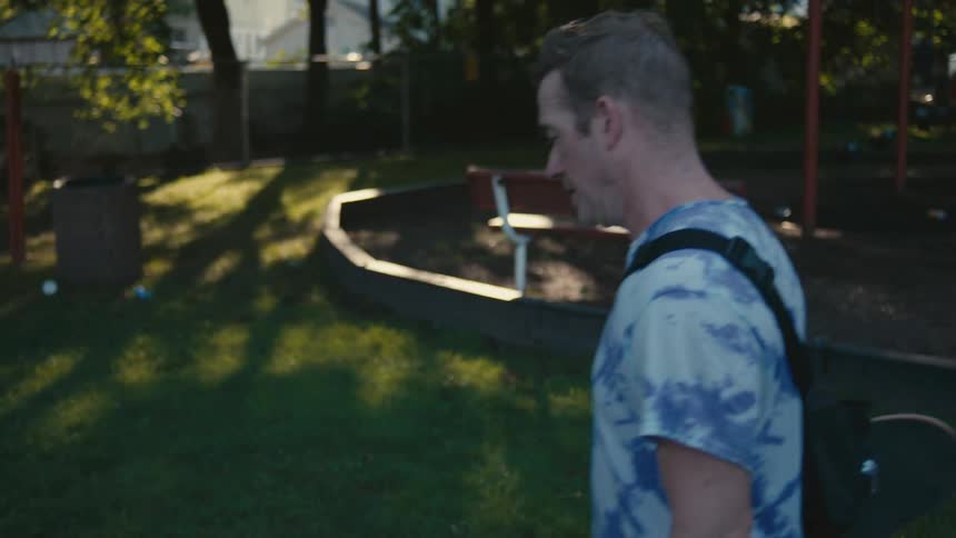 A man carrying a skateboard walks away from a public park