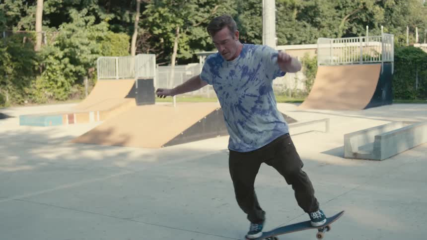 Man rides skateboard at skate park while another sits on platform
