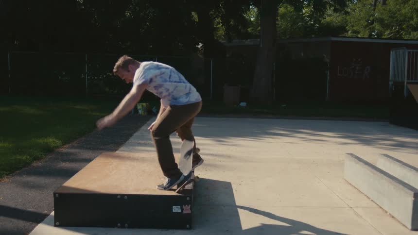 A man skateboarding in a public park jumps on to a ramp and falls off his board