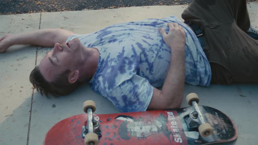 A man is laying on the sidewalk next to his skateboard