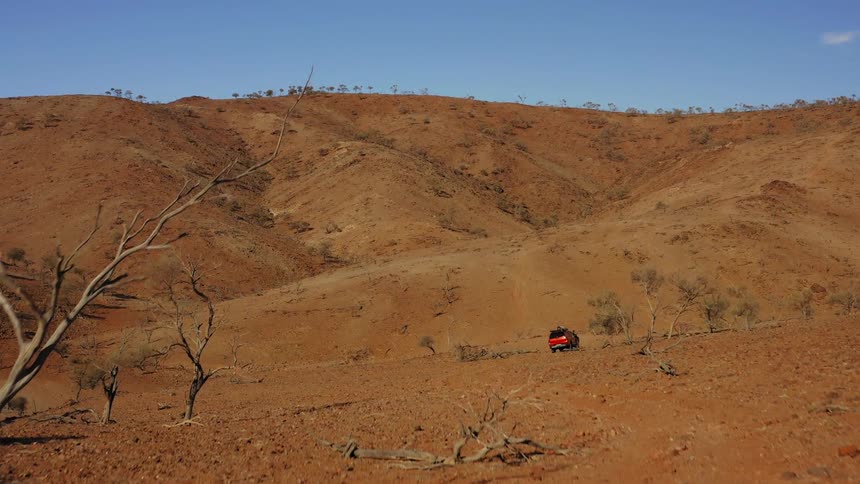 A vehicle travels off road across hills covered in rocks and sparse vegetation