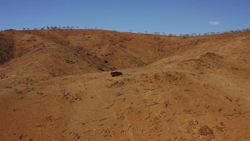 Aerial view of a red car climbing the slope of a hill on the desert