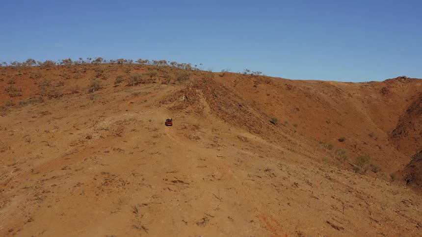 An aerial view of a vehicle driving up a dirt hill in nature