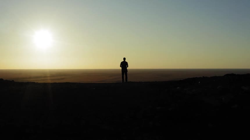 The sun shines down as a person stands and looks at the landscape