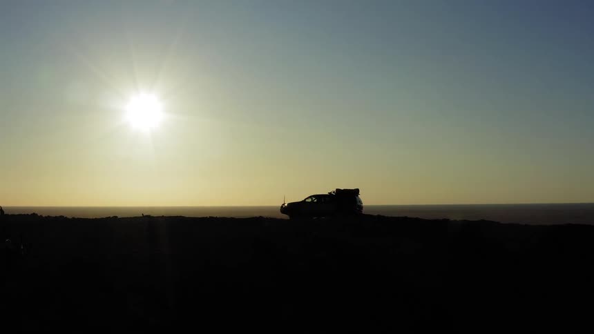 A four wheel drive drives along the top of a mountain at sunset