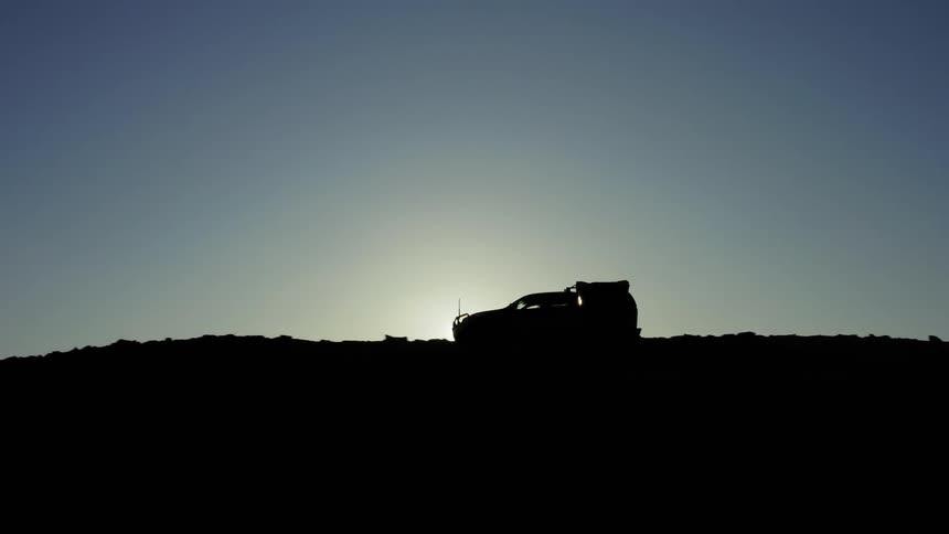 A vehicle drives along the top of a hill as the sun sets