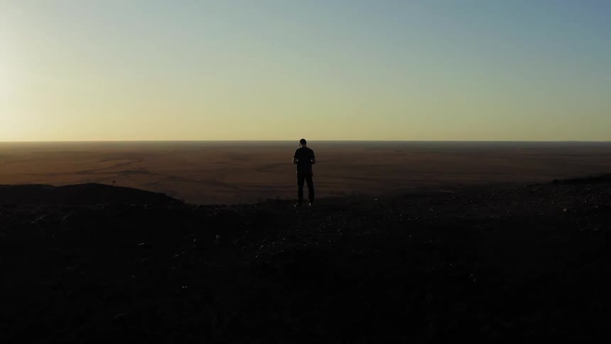 A man stands on the summit of a canyon at sunrise