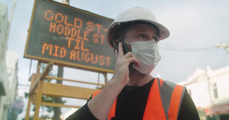 A road worker uses his smartphone to make a call while standing in front of a led traffic sign during the day