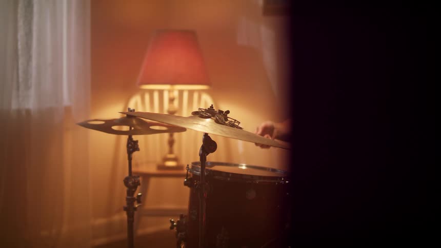 A hand holding a drum stick hits a drum set cymbal repeatedly