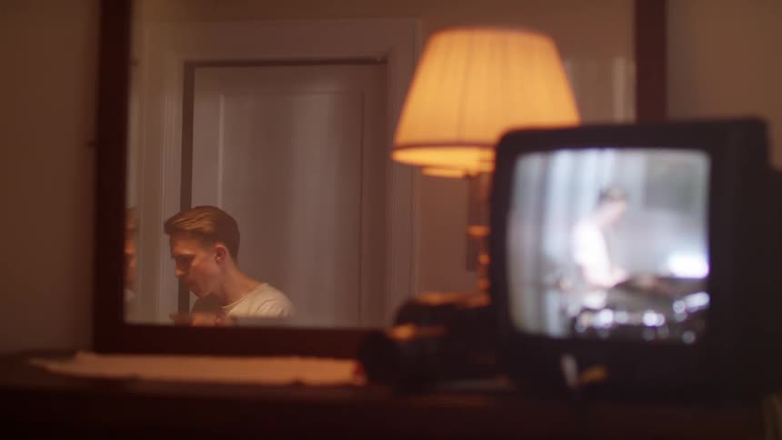 A reflection in the mirror shows a man playing the drums