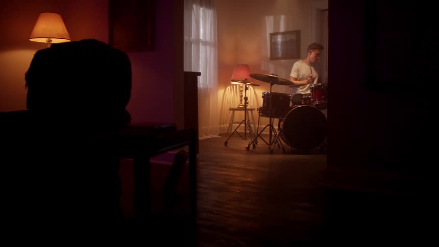 Male drummer plays a set of drums by hitting it with sticks in a dark room
