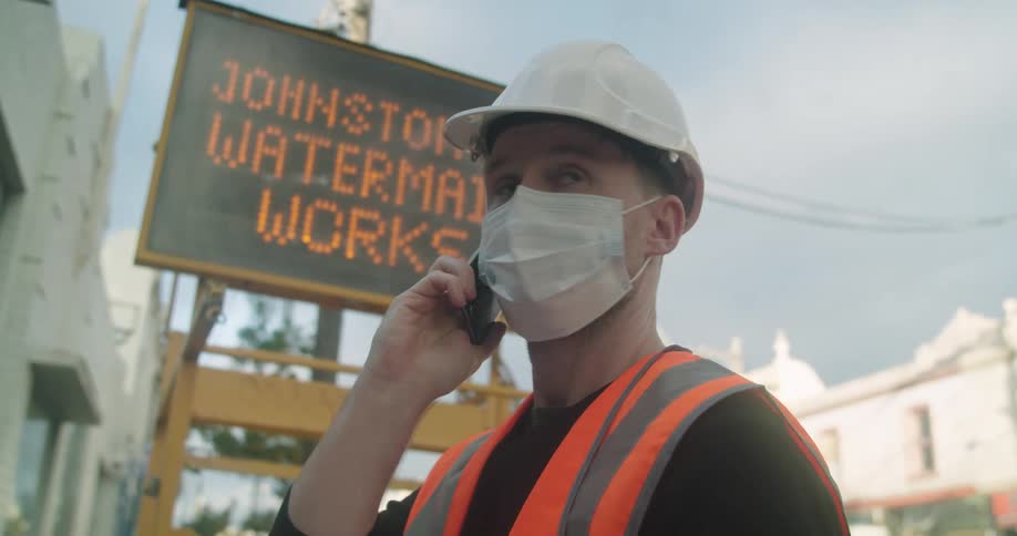 A construction worker talks on a cell phone while looking at a book