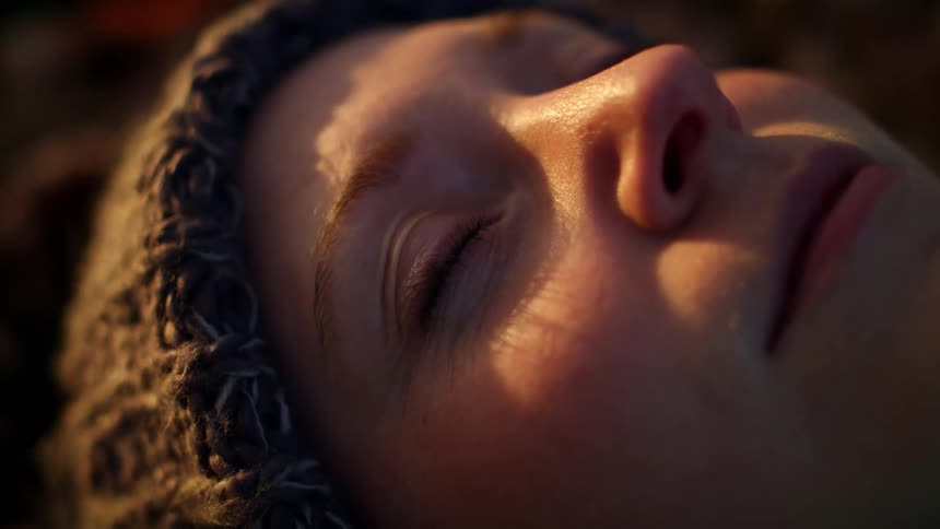 A woman wears a knit brown hat as she lies down outside and looks up at the sky