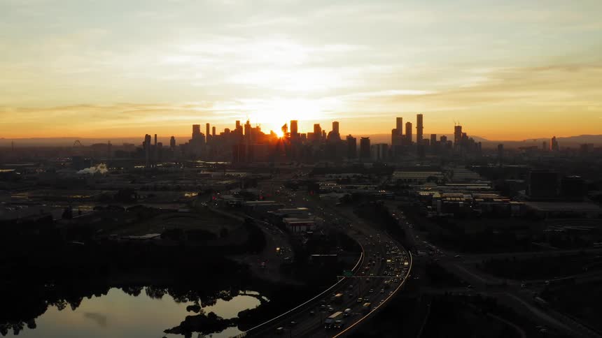Aerial view of vehicles driving on highways and the sun setting behind the high rise buildings on the horizon