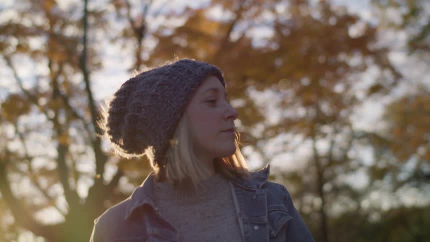 Woman wearing knit hat looks around at trees