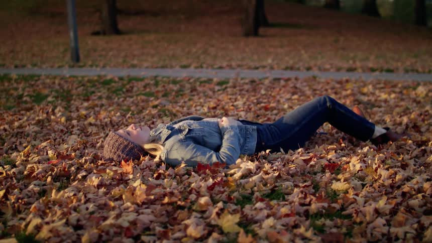 A woman is laying on the ground outdoors in fall