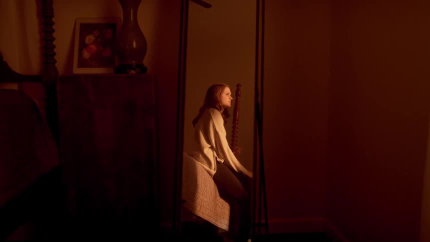 The reflection of a woman sitting on a bed lost in thought in a body length mirror