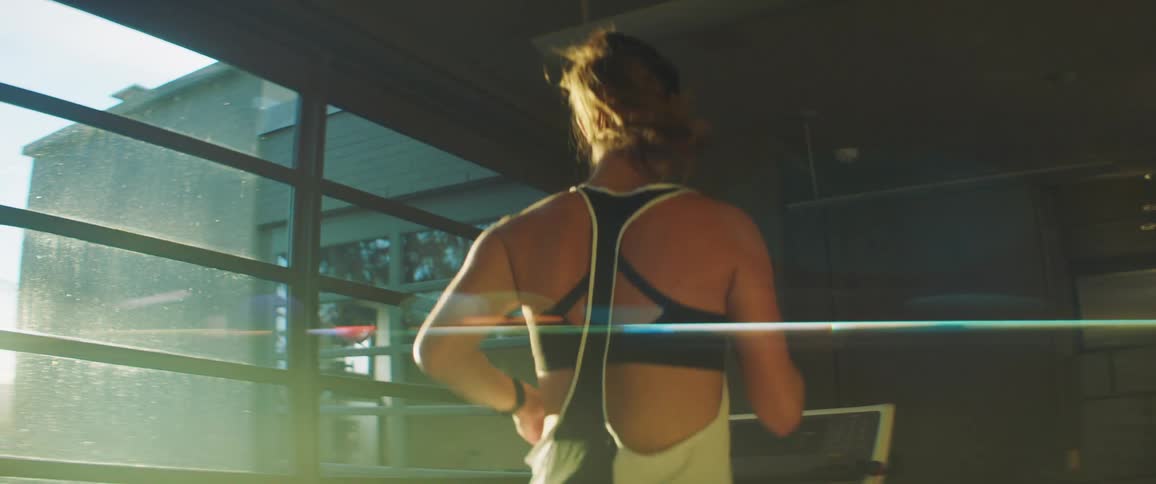 Woman runs on treadmill in bright sun shining through nearby window