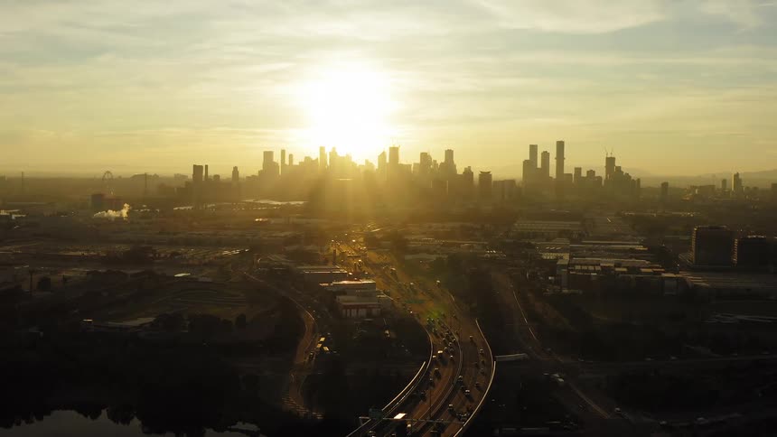 Aerial view of vehicles driving on highways and high rise buildings silhouetted against the sunset