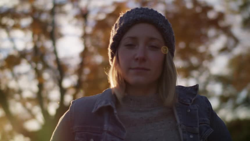 A young woman looks into the camera while standing under a tree with yellowing leaves