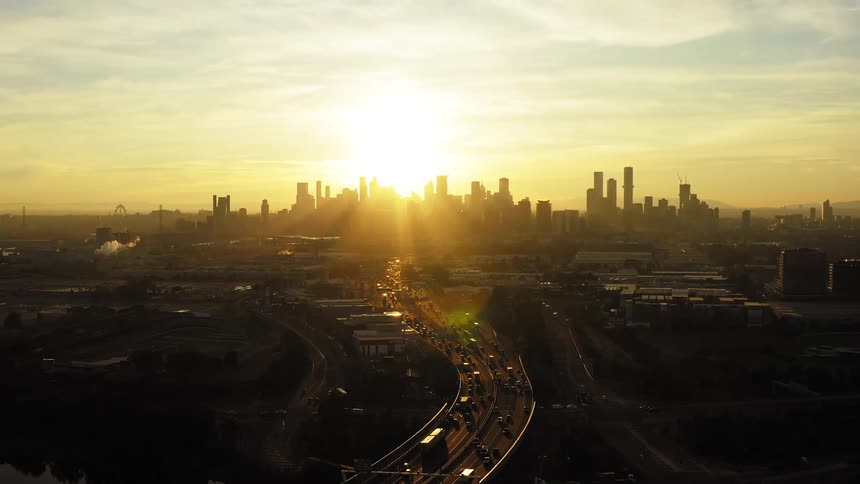 Aerial view of vehicles driving on highways and high rise buildings silhouetted against the sunset