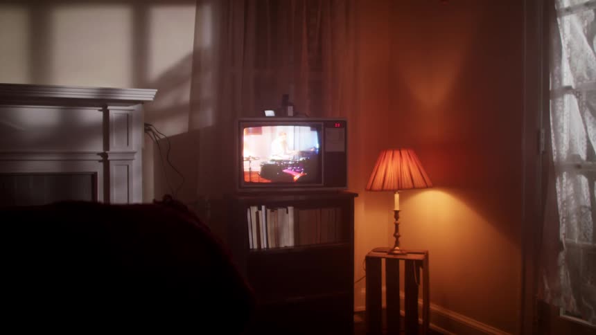 An old crt television in a living room displays a man playing the drums