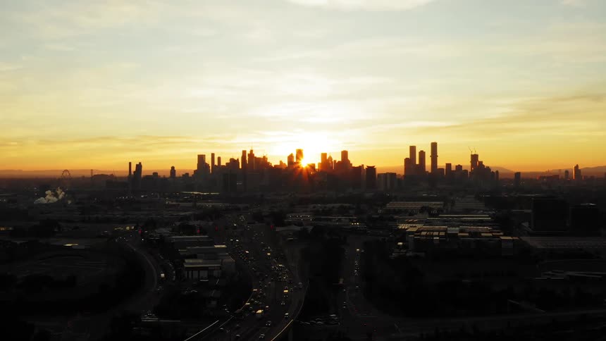 Aerial view of vehicles driving on highways and high rise buildings silhouetted against the sunset