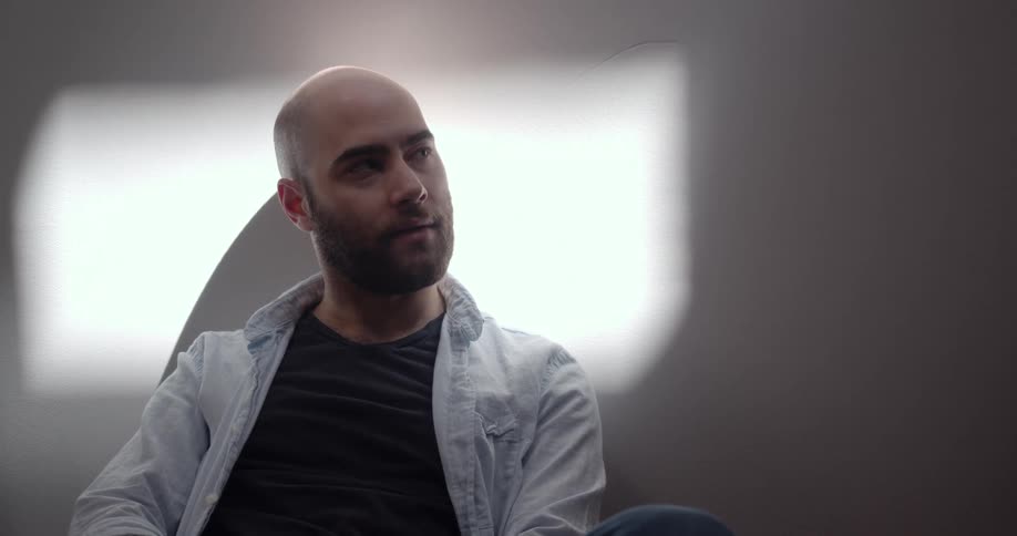 A white man sitting in a room looks around