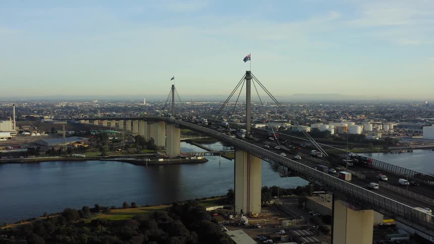A suspension bridge spans a river and numerous vehicles drive over it