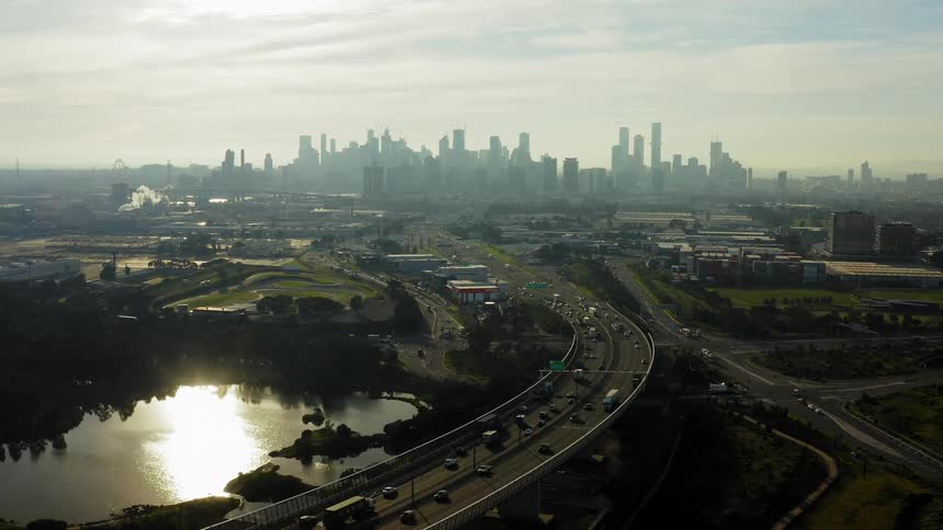 An aerial view of vehicles driving on a city street with the downtown skyline in the background