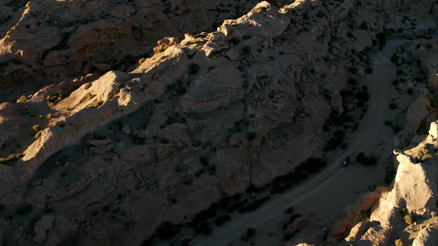 A motorcyclist rides down a narrow dirt road in a tall canyon