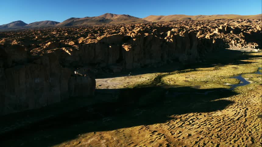 A narrow creek runs through dry ground at the bottom of a canyon