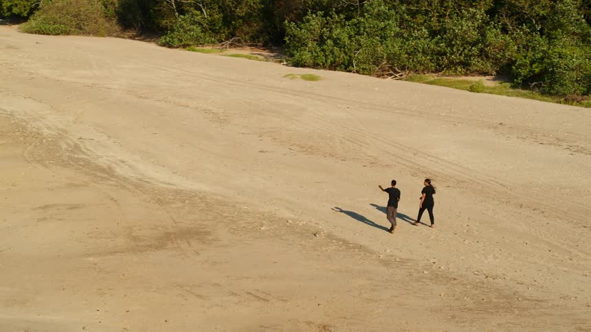 Aerial view of two women with black t shirts walk on the beach