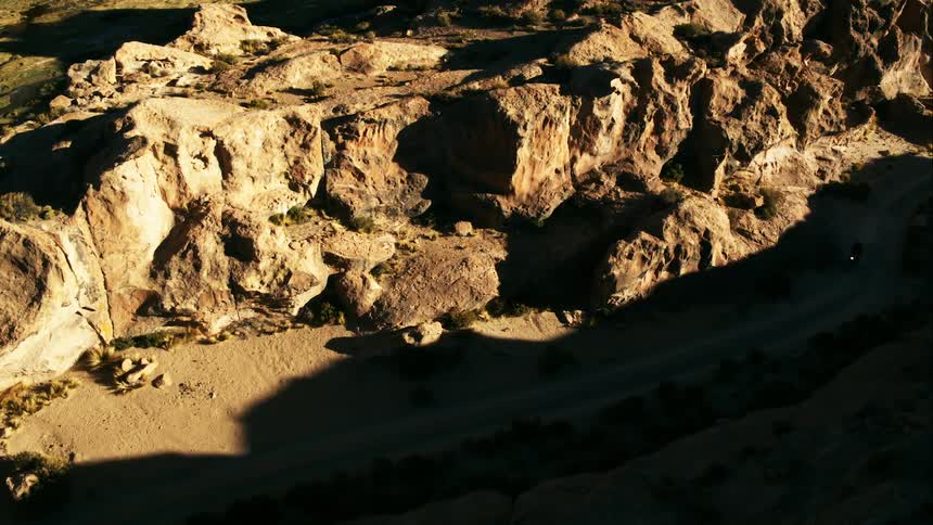A biker rides a motorcycle down a dirt road through a canyon in the badlands during the day