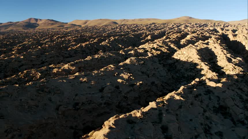 Creek runs through ravine in broken rough terrain reaching hills on horizon