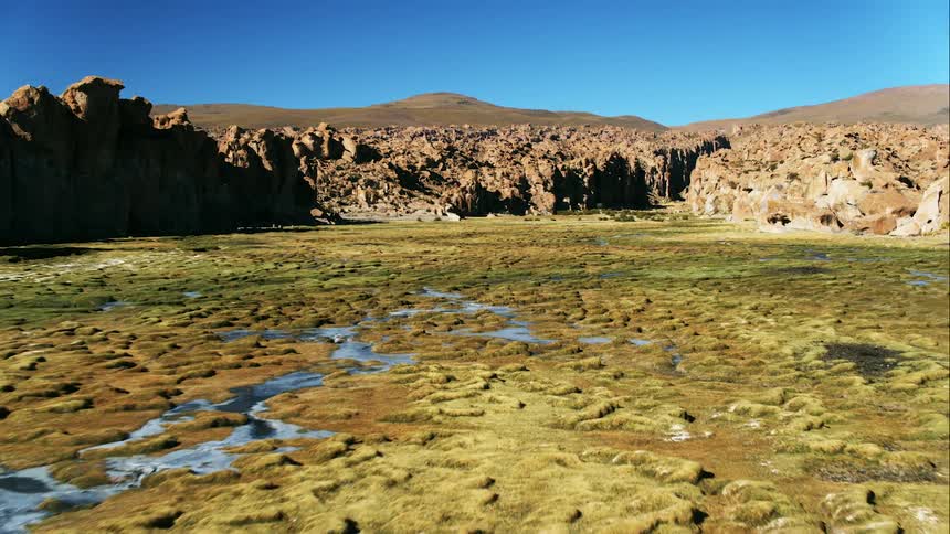 A canyon with wetlands with a mountain range the sky and clouds in the background