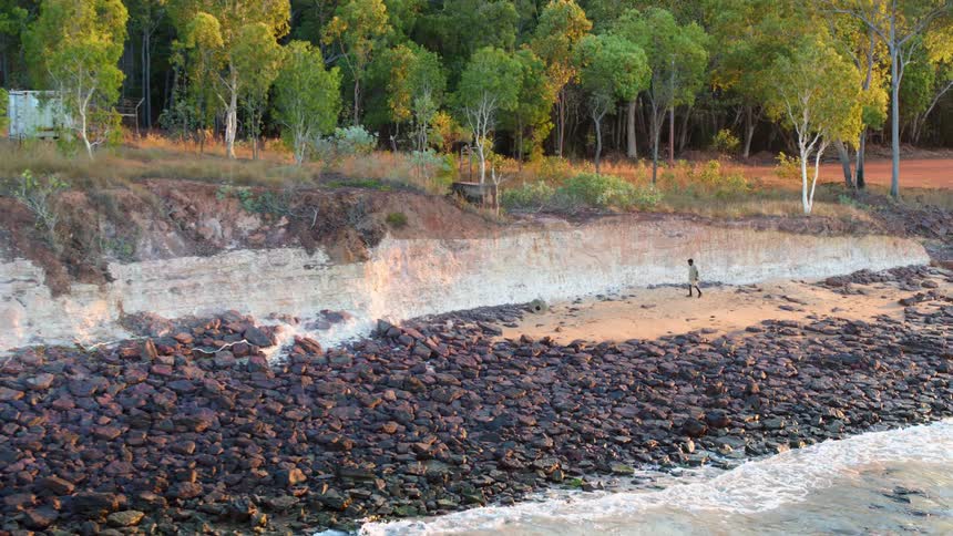 A person walks along a beach covered in stones during the day
