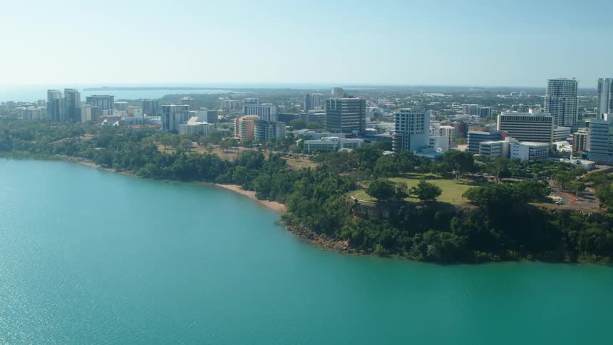 Trees line shore near park while city stretches to horizon on sunny day