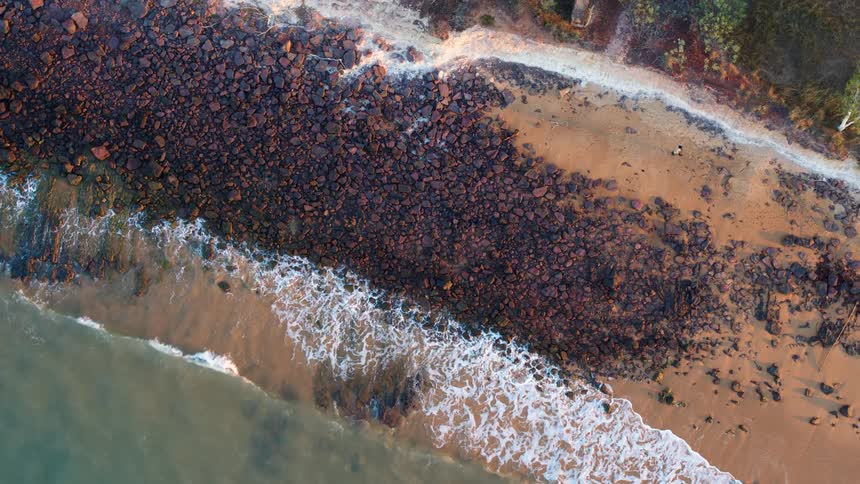 Aerial view of ocean waves breaking against the rocky shore