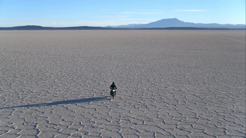 Aerial view of a person riding a black motorcycle through the desert near the mountains