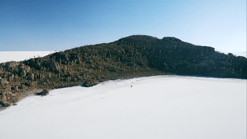 Person rides past vegetation covered hill under clear blue sky