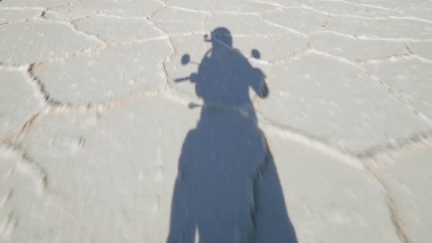 A shadow of a person on a motorcycle driving across a desert