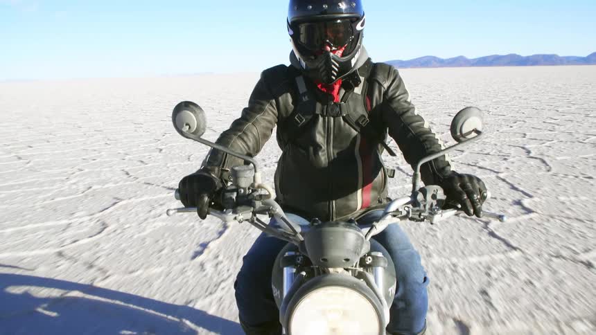 Motorcyclist with a helmet a black leather jacket and jeans rides a motorcycle across the large white sand desert