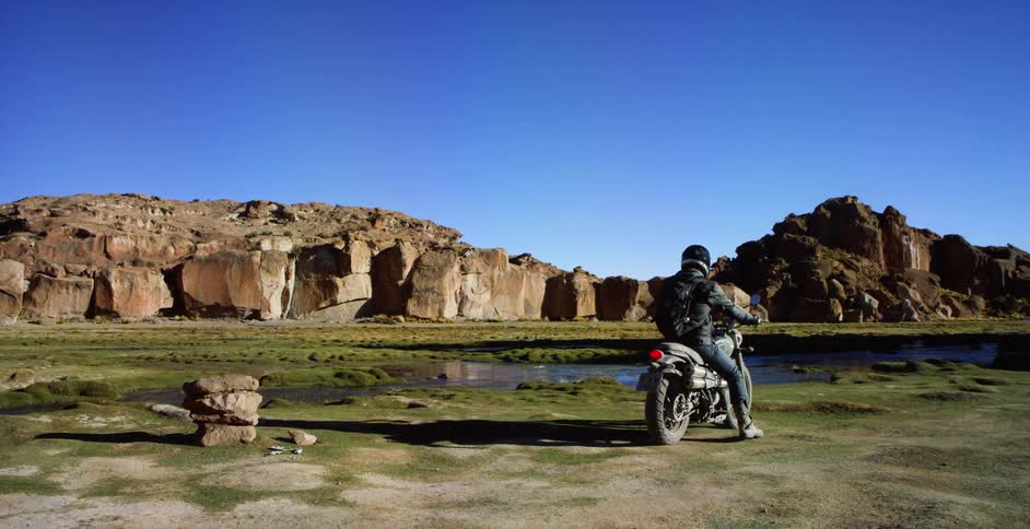 A person sits on his motorcycle near the small stream