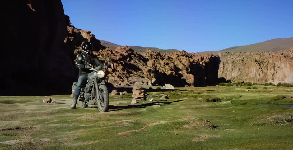 A person sits on a motorcycle in grassy area with canyons surrounding them
