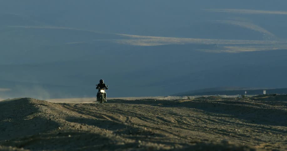 A biker rides a motorcycle through the soil of the desert on a sunny day