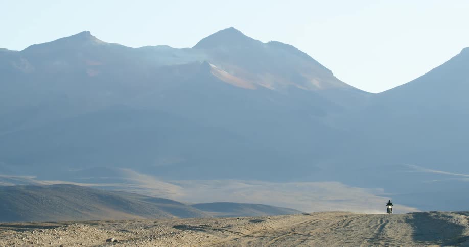 A motorcyclist rides through the empty lands of a desert during the day